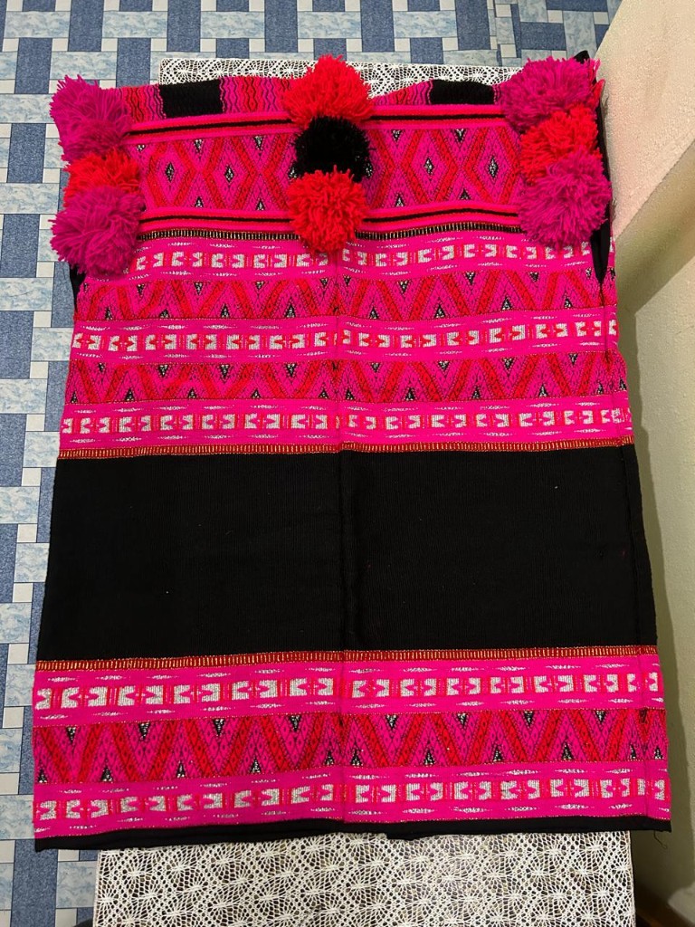 Colourful hand-woven Mishmi textile with geometric patterns and yarn pom-poms.